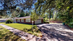 A single-story house with a garage, surrounded by a well-maintained lawn and tall trees. - Grace Cottage 3 bedrooms, 2 bathrooms (Jekyll Island)