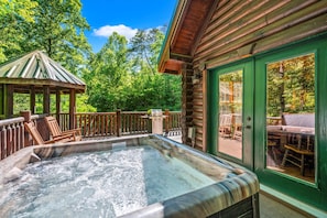 A hot tub on a wooden deck with a gazebo and outdoor furniture.