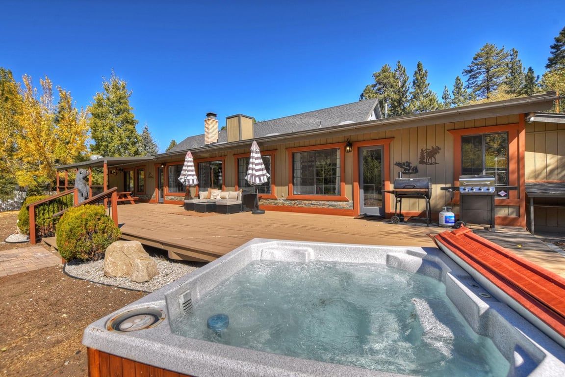 Un jacuzzi en una terraza de madera, un área de estar techada al aire libre y una parrilla.
