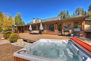A hot tub on a wooden deck, a covered outdoor seating area, and a barbecue grill.