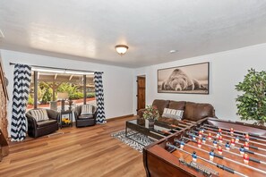 Una sala de estar con mesa de futbolín, sofá, mesa de centro y un amplio ventanal con cortinas.