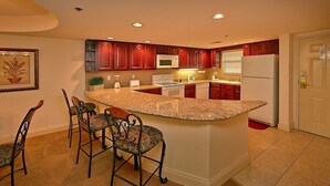 Una cocina con isla de granito, taburetes de bar, armarios de madera y un refrigerador.