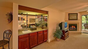 Una sala de estar con chimenea, televisor y un área de cocina con lavaplatos y armarios.