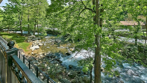 Un río que atraviesa un área ajardinada con árboles y rocas, visto desde un balcón con barandilla.