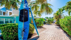 Una tavola da surf blu appoggiata a un edificio con una palma e un vialetto lastricato.