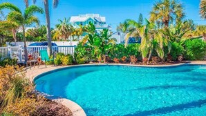 Piscina cristallina blu circondata da lussureggiante vegetazione e palme, con una recinzione bianca e una casa sullo sfondo.