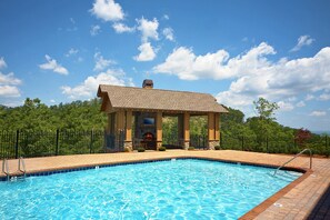 Une piscine dotée d’un pavillon couvert, entourée d’une terrasse en briques et d’une clôture en métal.