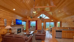 Una cabaña amplia con chimenea, sofás de cuero, televisor y zona de cocina.
