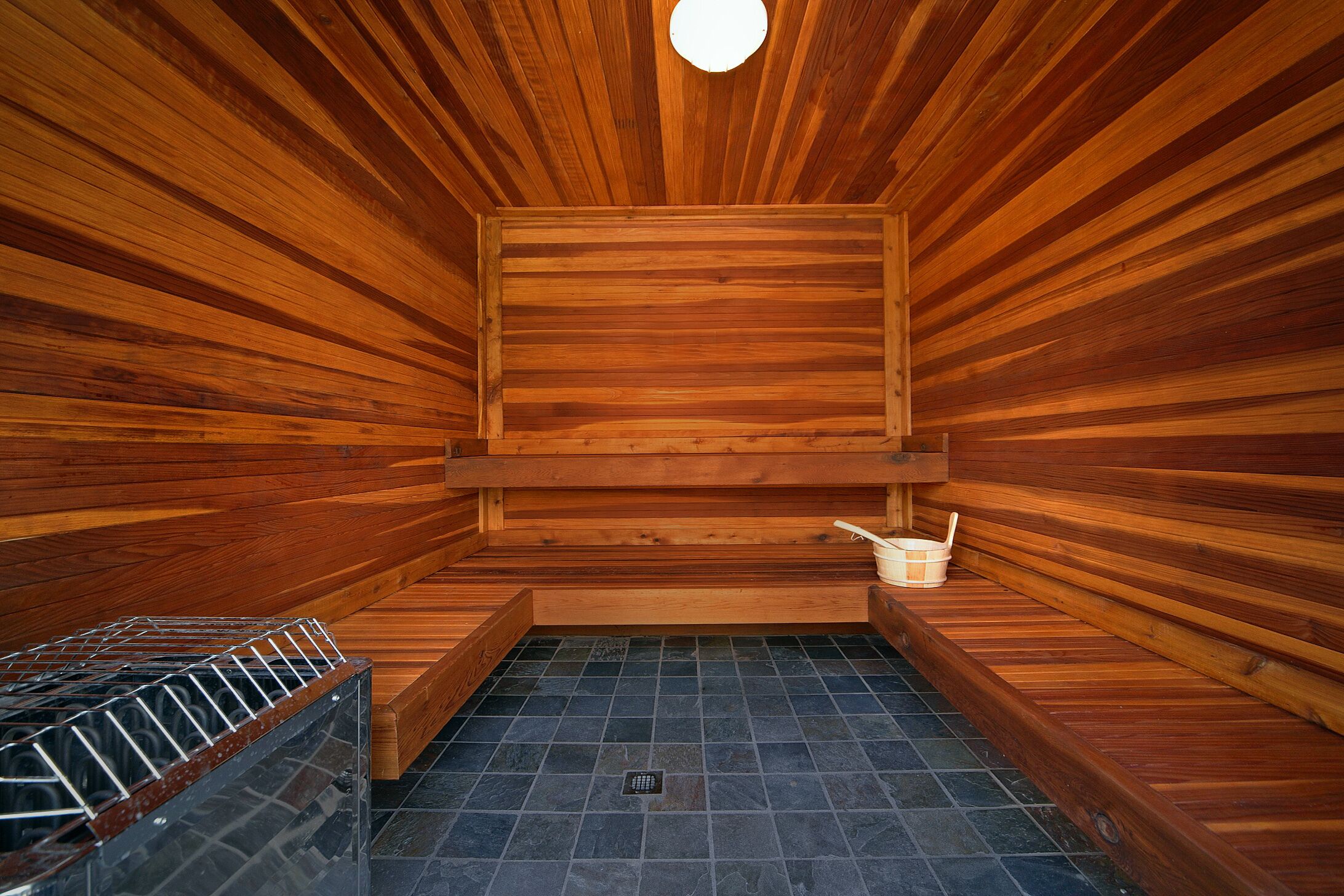 Eine Sauna mit Holzwänden und -bänken, gefliestem Boden und einem Metallregal.