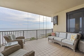 En balkon med fletningsmøbler, et glasbord og havudsigt.