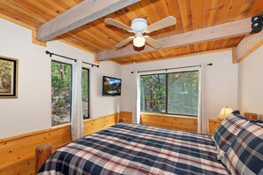 Une chambre à coucher avec un lit, un ventilateur de plafond, une télévision et de grandes fenêtres.
