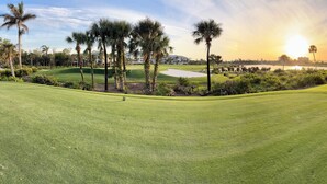 Un parcours de golf offrant une vue sur le coucher de soleil, bordé de palmiers et comprenant un plan d’eau.