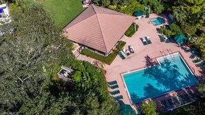 Vue aérienne d’un complexe hôtelier doté d’une piscine, de chaises longues et d’un patio couvert.