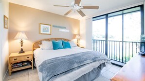 Une chambre à coucher comprenant un lit, deux tables de chevet avec des lampes, un ventilateur de plafond, un balcon avec une rambarde et une fenêtre.
