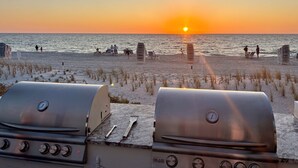 Une plage avec deux barbecues, un coucher de soleil et l’océan.