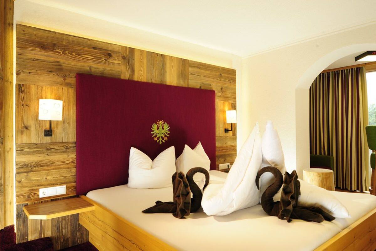 A hotel room with a wooden headboard, a red accent wall, and a bed with white bedding and decorative swan pillows.