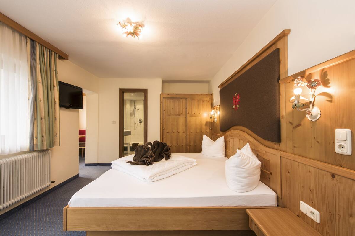 A hotel room with a wooden bed, a television, a bathroom with a shower, and a wooden wall with a light fixture.