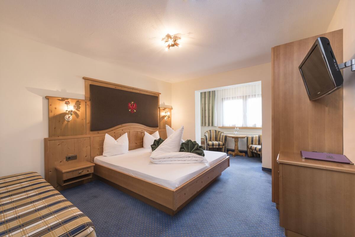A hotel room with a wooden bed, a small bedside table, a chair, a desk, and a TV mounted on the wall.