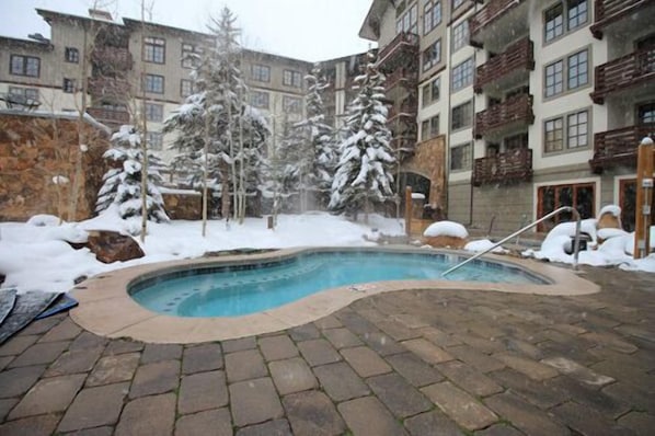 Ein Pool mit Steinrand, umgeben von schneebedeckten Bäumen und Gebäuden.