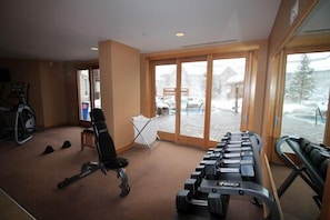 Ein Fitnessstudio mit Trainingsgeräten, Laufband und großen Fenstern mit Blick auf eine verschneite Landschaft.