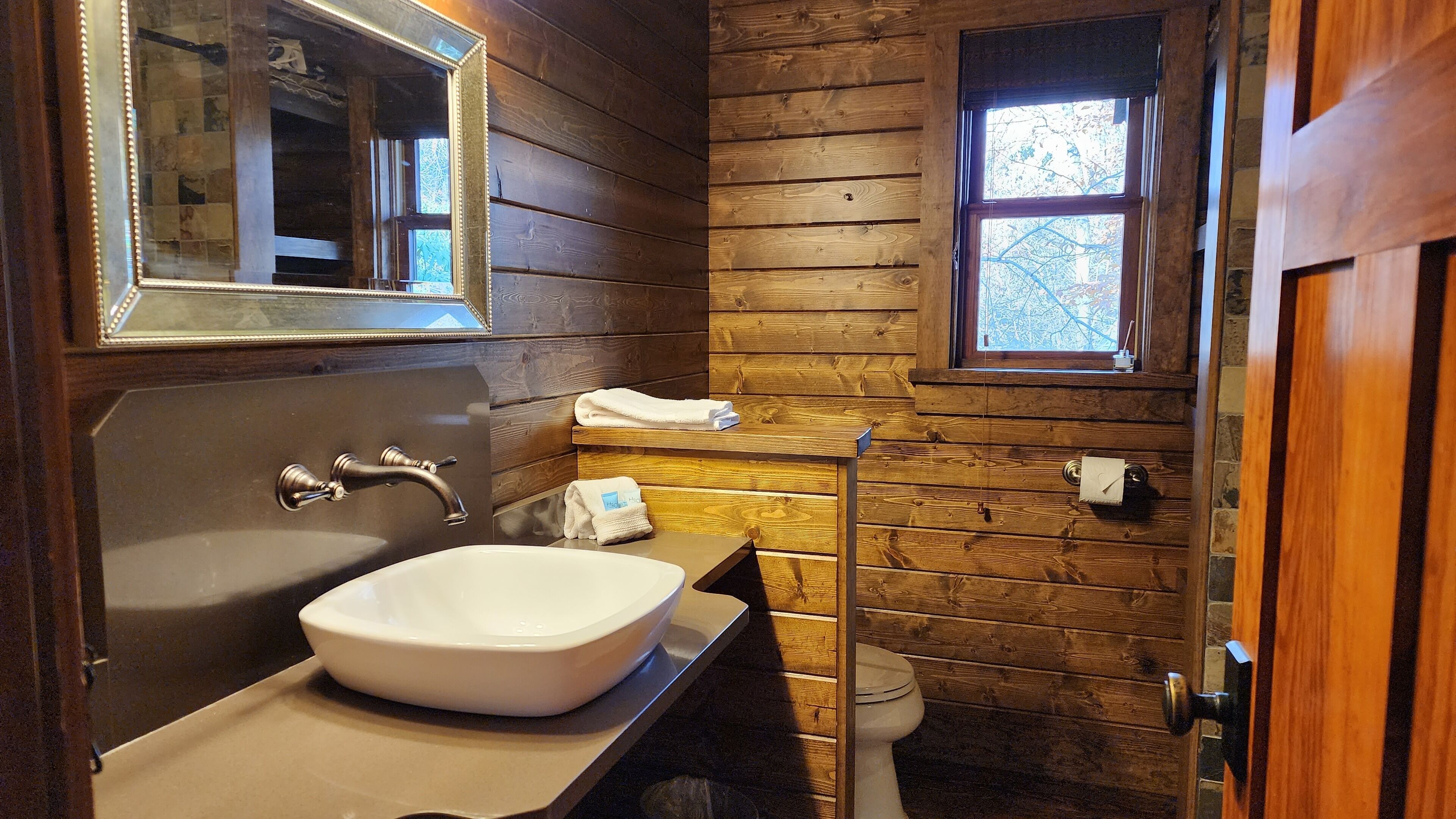 Un bagno con una vasca da bagno ampia, uno specchio, una finestra e pareti in legno.