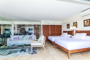 Une chambre d’hôtel avec un lit, un canapé, une chaise, une table en verre et un coin cuisine à l’arrière-plan.