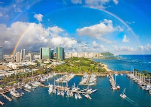 A marina with numerous boats docked, a city skyline with modern buildings, and a rainbow in the sky. - Ocean Breezes + Yacht Harbor Views at the Ilikai Hotel! (Honolulu)