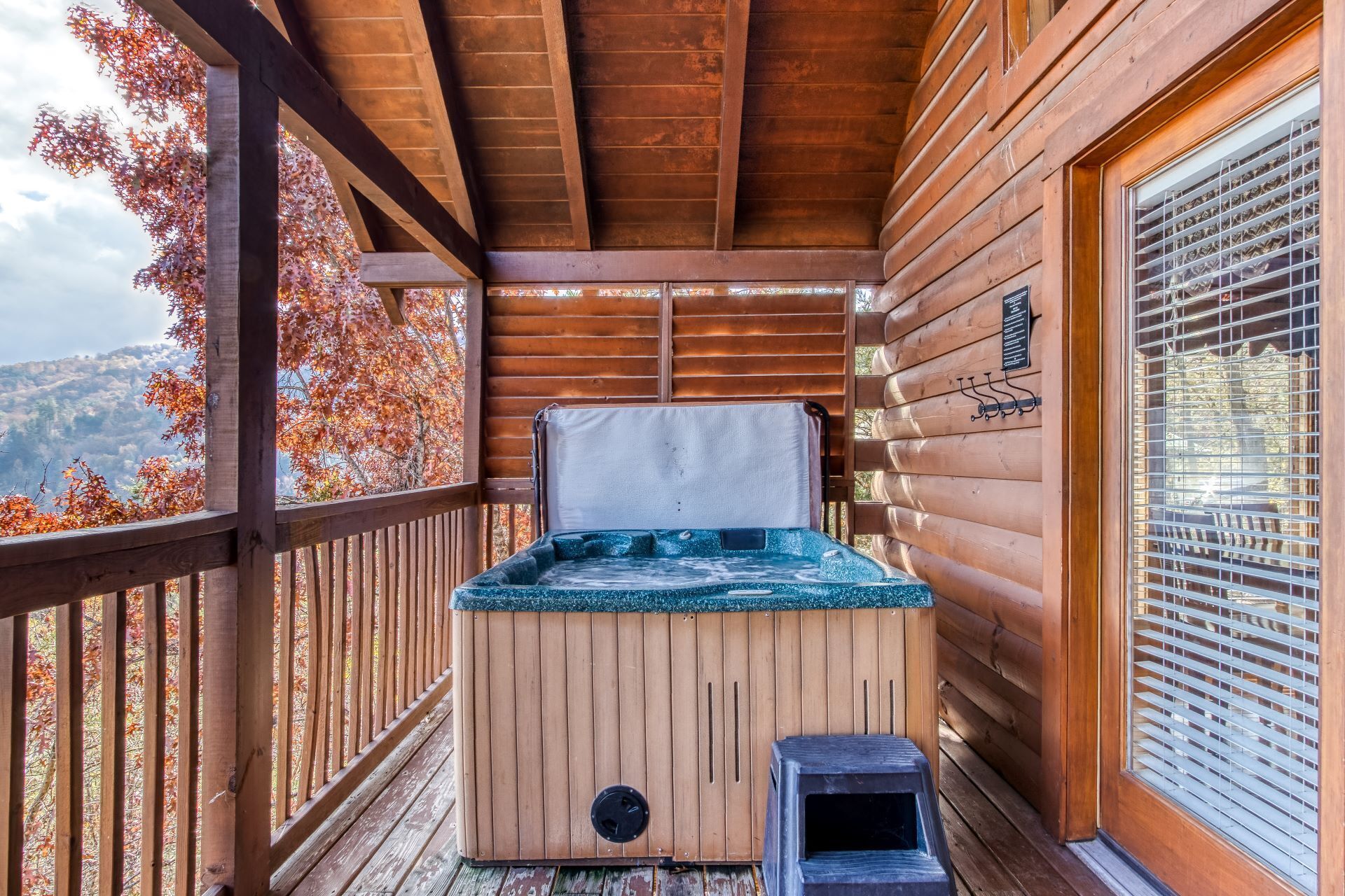 Eine Holzhütte mit Whirlpool, einer Holzterrasse und Blick auf Herbstbäume.