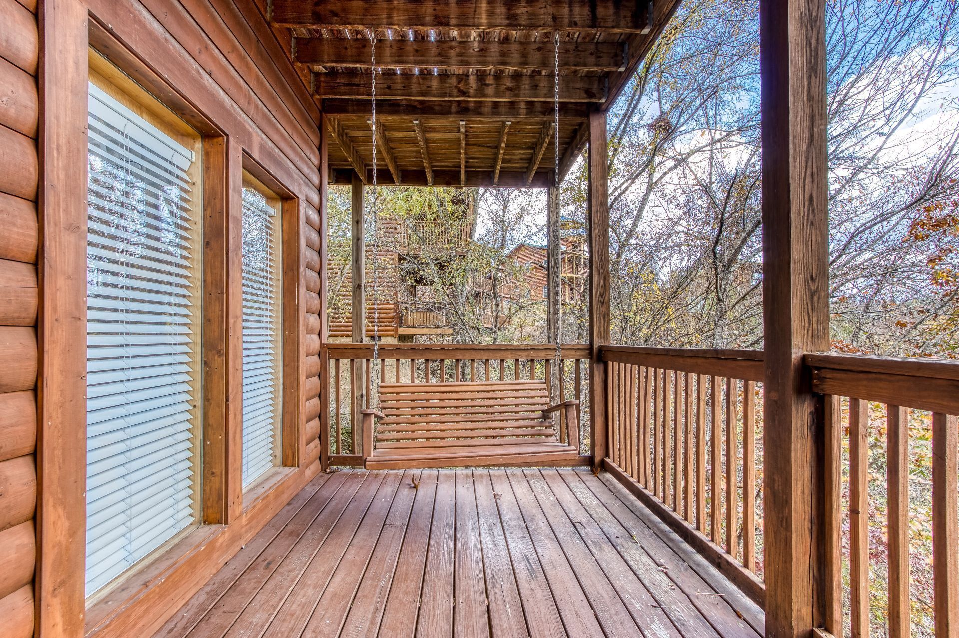 Una cabaña de madera con un porche cubierto, un banco y vistas del bosque circundante.