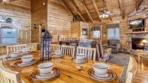 L’intérieur chaleureux d’un chalet avec une table à manger en bois, des bols et des assiettes, une cheminée et un téléviseur fixé au mur.