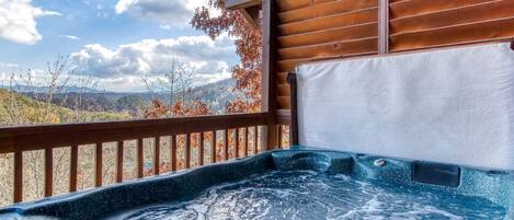 A hot tub with a wooden deck and a view of mountains.