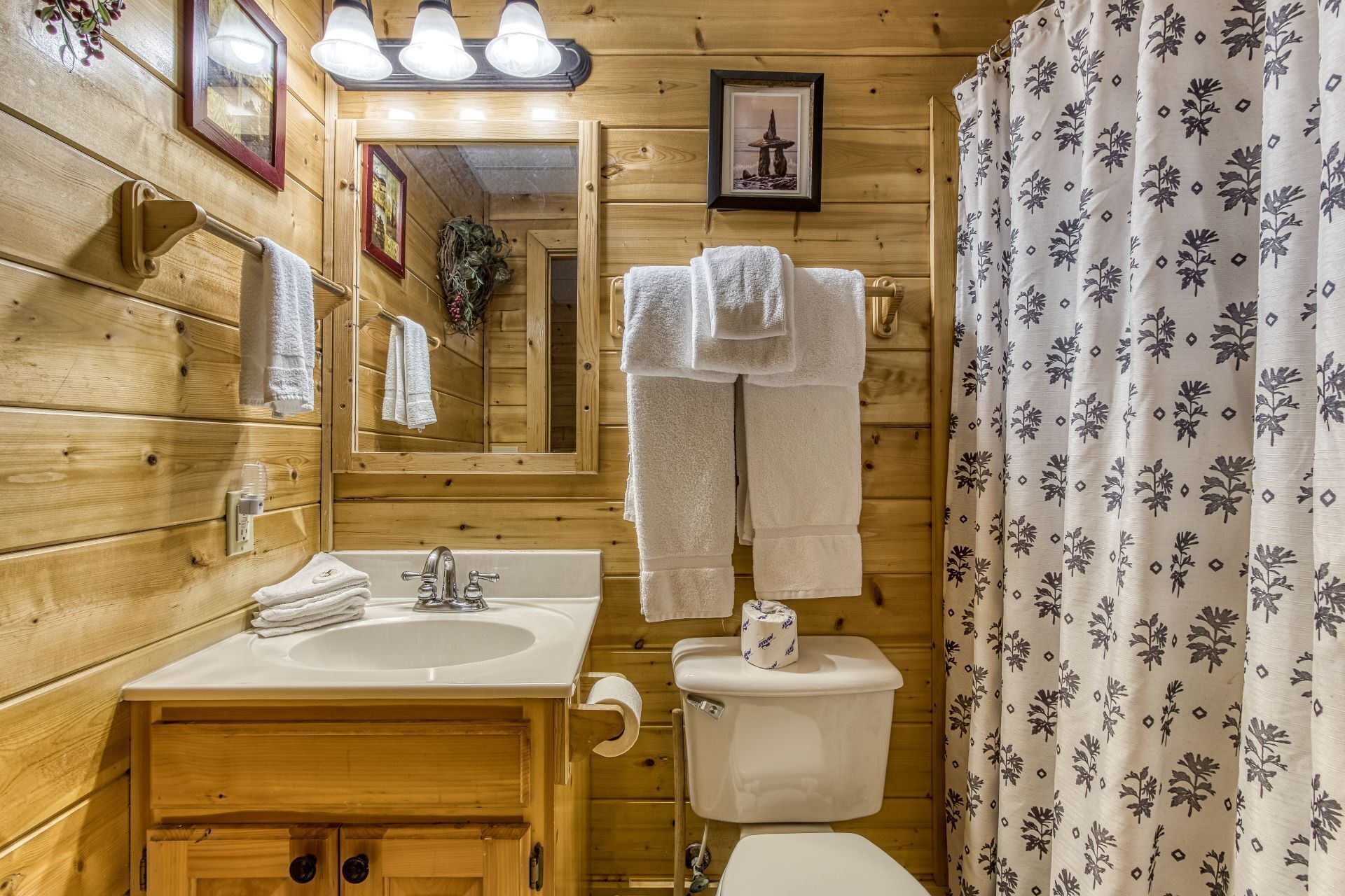 Baño de cabaña de madera con lavamanos, inodoro y cortina de ducha.