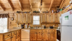 Une cuisine de style rustique, avec des meubles en bois, un réfrigérateur blanc et une fenêtre équipée de stores.