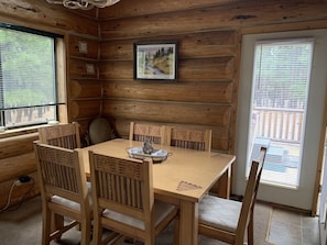 A wooden cabin interior with a dining table and six chairs, a framed picture on the wall, and a window with blinds. - Hurd Cozy Log Cabin (Greer)