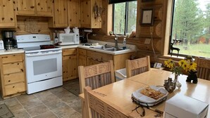 A wooden cabin kitchen with a stove, sink, and dining table. - Hurd Cozy Log  Cabin (Greer)