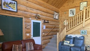 A log cabin interior with a brown leather sofa, a blue leather sofa, and a wooden coffee table. - Hurd Cozy Log  Cabin (Greer)