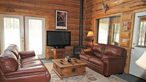 A log cabin interior with a brown leather sofa, a wooden coffee table, a television, and a fireplace. - Hurd Cozy Log  Cabin (Greer)