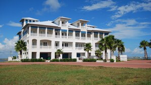 Een meerlaags hotel met balkons, palmbomen en een helder uitzicht op de oceaan.