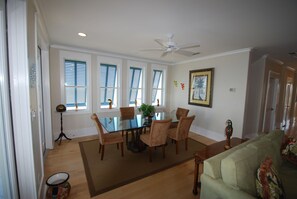 A dining area with a glass table surrounded by chairs, a ceiling fan, and windows with blinds. - Kokopelli!  Breathtaking Sunset Views! Lookout Tower! 4 Bedroom Villa on the Bay (South Padre Island)