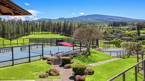Una cancha de tenis con red, rodeada por una cerca y un camino que lleva a un área de descanso.