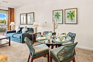A dining area with a glass table, green upholstered chairs, and a blue sofa with decorative pillows.