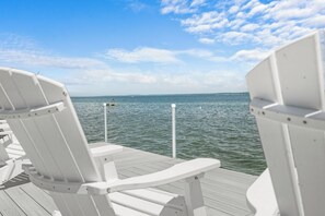 A deck with white chairs facing a calm body of water under a clear sky.