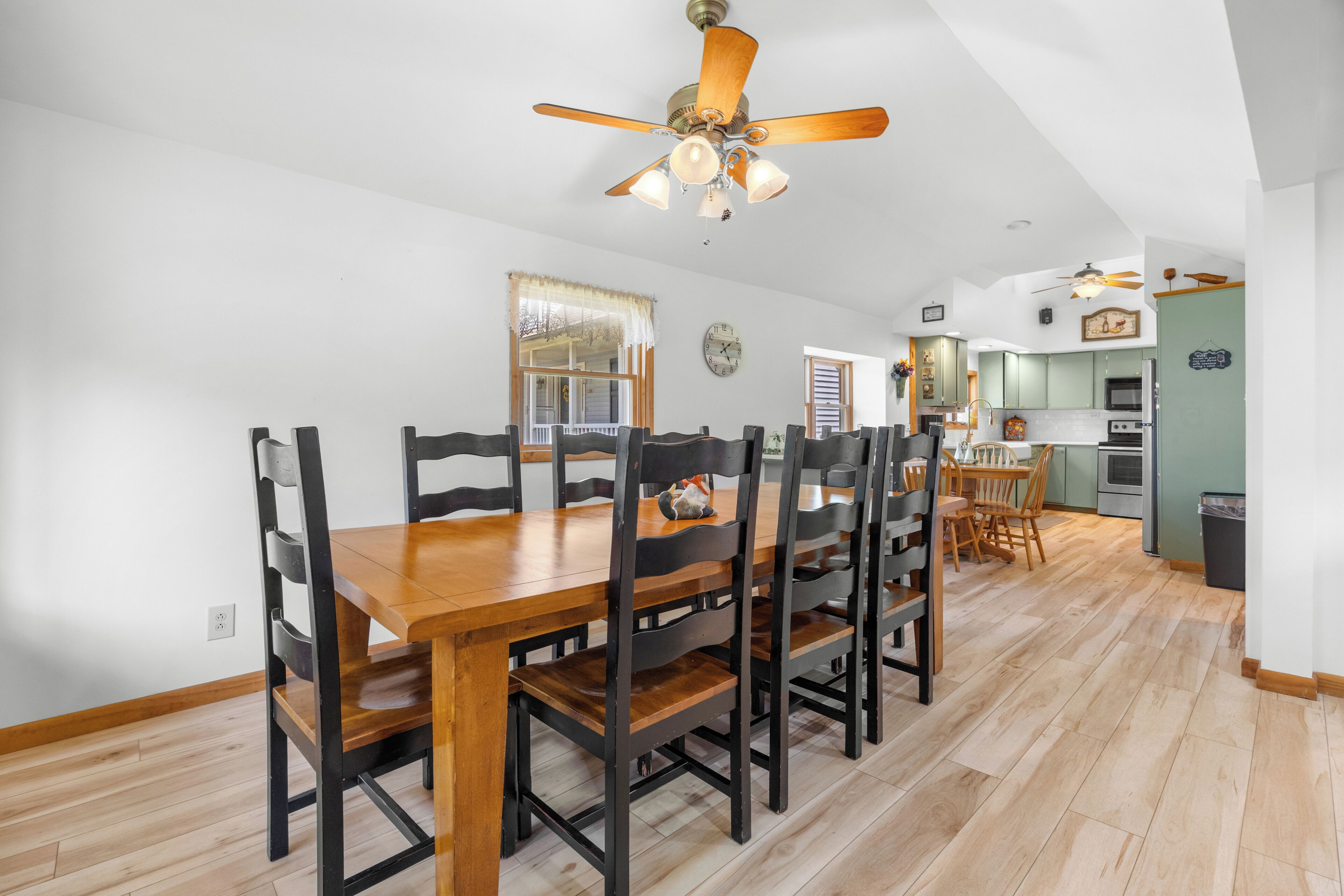 A dining area with a wooden table and chairs, a ceiling fan, and a kitchen in the background.