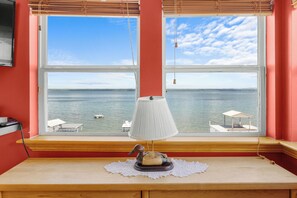 A room with a large window overlooking a body of water, a wooden table with a lamp, and a small decorative item.