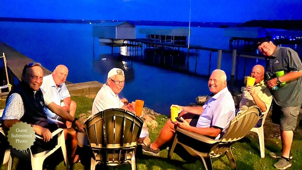 A group of people seated outdoors at a lakeside venue with a dock and pier in the background.