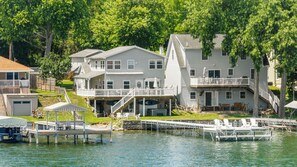A waterfront property with a dock, a covered deck, and a two-story house with multiple windows and balconies.