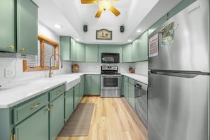 A kitchen with green cabinets, a stainless steel refrigerator, a microwave, an oven, and a ceiling fan.
