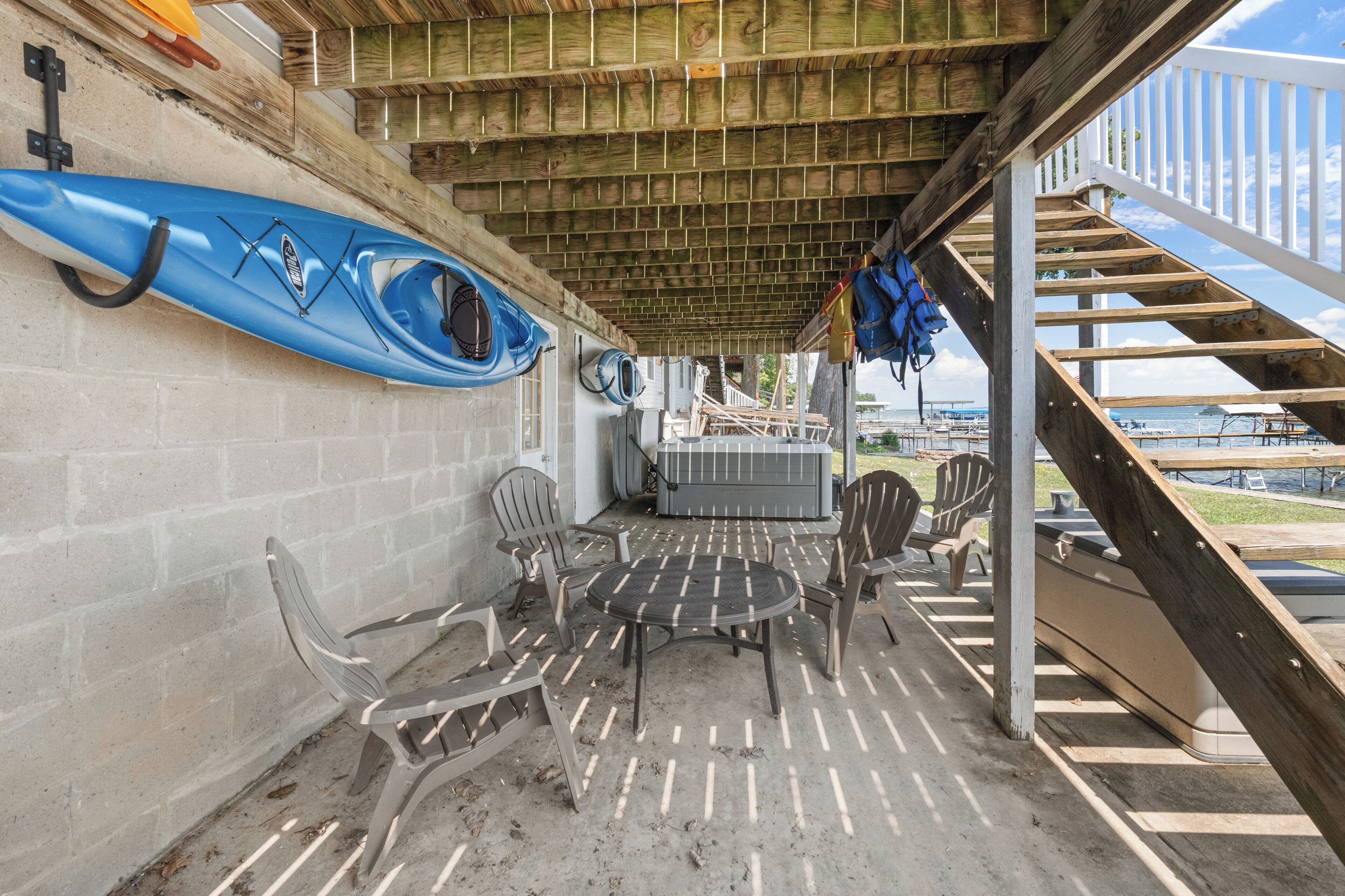 Un espace extérieur abrité, équipé d’une table et de chaises, de kayaks et d’un escalier menant à une terrasse.