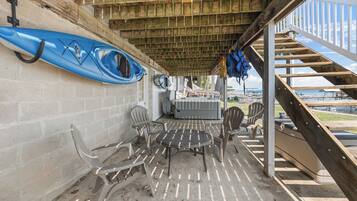 Un espace extérieur abrité, équipé d’une table et de chaises, de kayaks et d’un escalier menant à une terrasse.