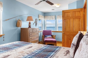 A room with a bed, a dresser, a chair, a window with a view, and a ceiling fan.